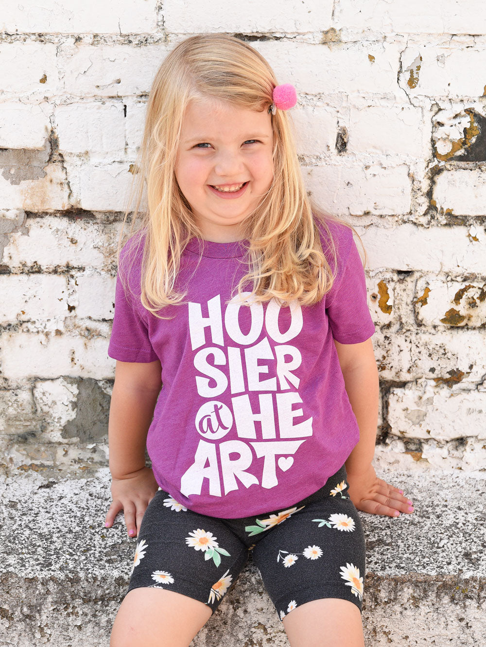 Hoosier at Heart magenta heather youth t-shirt on model in front of white brick wall